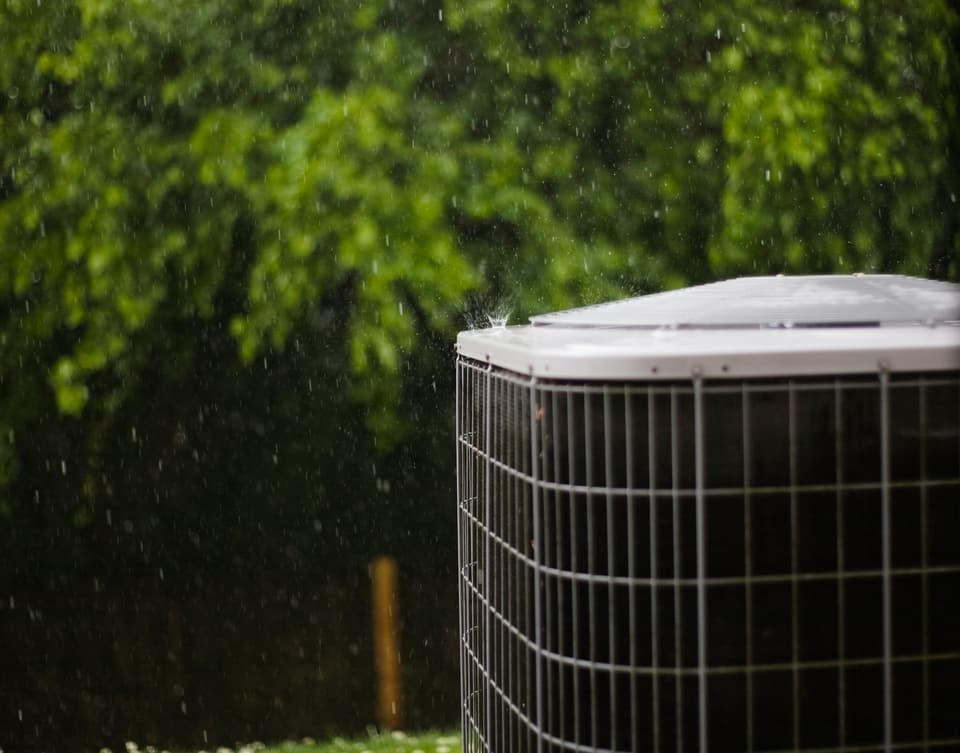 An outdoor air conditioning condenser in the rain, with trees behind it