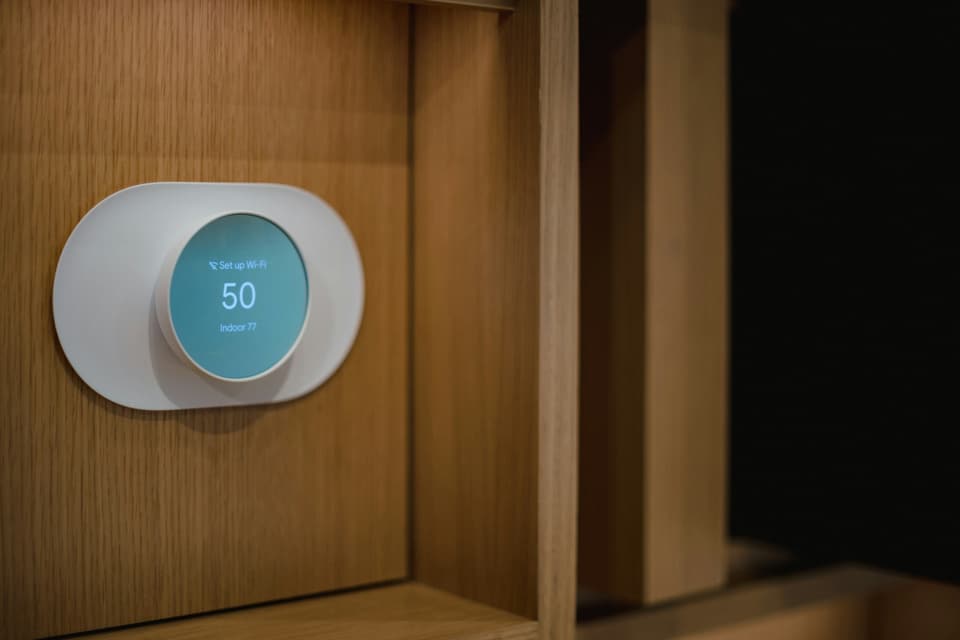 A round smart thermostat on a wooden wall panel, its display reading 50 with the room at 77 degrees